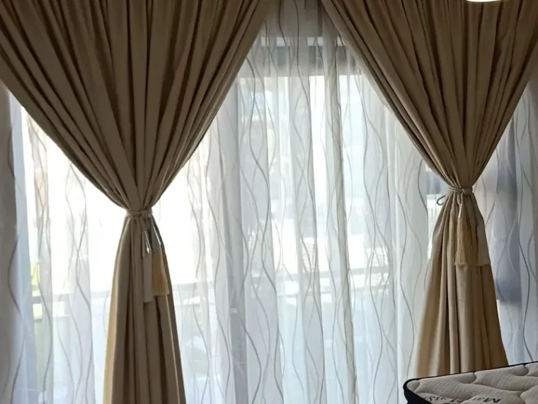Beige curtains with tassel tie-backs over patterned white sheers in a Cape Town bedroom