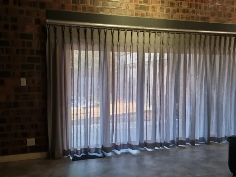Silver sheer curtains with a dark border in a Cape Town brick-wall lounge