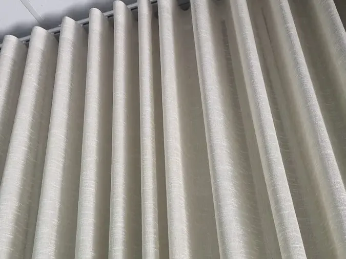 Cream wave curtains on a ceiling track, close-up detail