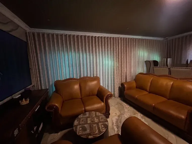 Greige wave-pleat curtains fitted across a Cape Town lounge with leather sofas