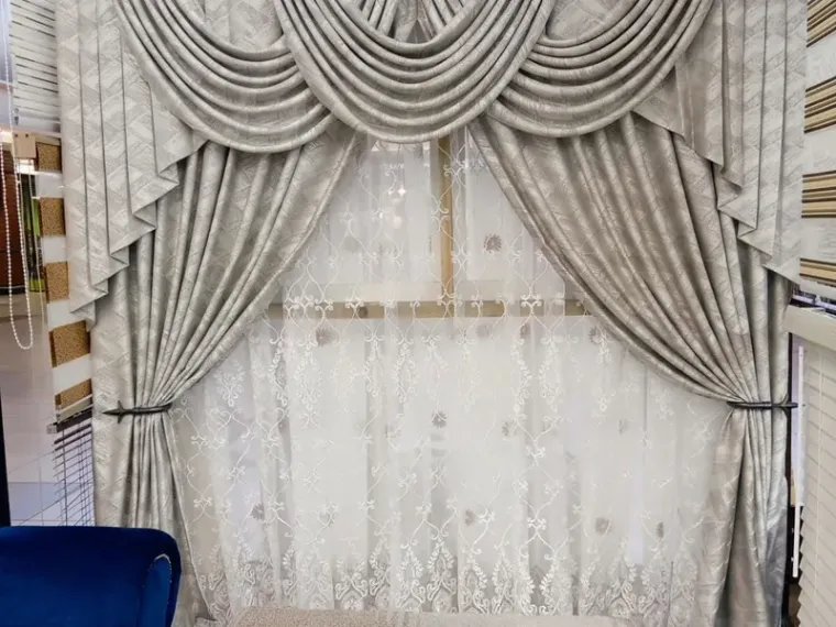 Silver-grey swag pelmet curtains over embroidered sheers on display at the Curtain Zone showroom
